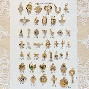 May include: A collection of gold-colored charms with various designs, including hearts, crosses, crowns, and locks. Some charms feature gemstones and intricate detailing. The image includes the text "@SantomaroDesign" and numbered labels for each charm.