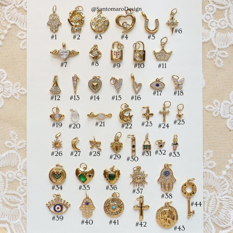 May include: A collection of gold-colored charms with various designs, including hearts, crosses, crowns, and locks. Some charms feature gemstones and intricate detailing. The image includes the text "@SantomaroDesign" and numbered labels for each charm.
