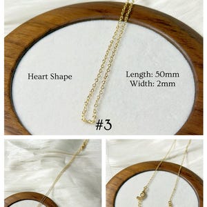 Op de afbeelding: Een delicate goudkleurige ketting met een hartvormige hanger. De ketting wordt gepresenteerd op een wit oppervlak in een houten frame. Tekst op de afbeelding luidt "Heart Shape", "Length: 50mm", "Width: 2mm" en "#3".