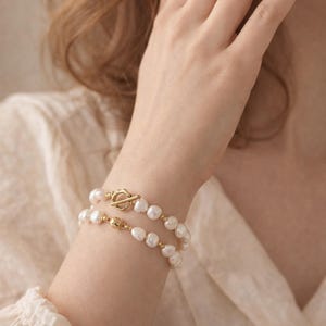 May include: A double-strand pearl bracelet with a gold clasp. The bracelet features irregular, white pearls and a gold toggle clasp. The design is elegant and classic, suitable for various occasions. The bracelet is a piece of jewellery.
