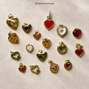 Könnte beinhalten: Eine Sammlung goldfarbener herzförmiger Anhänger mit verschiedenen Designs, darunter Edelsteine, Sterne und aufwendige Details. Einige Anhänger weisen rote, grüne und weiße Akzente auf. Die Anhänger werden auf einer neutralfarbenen Oberfläche präsentiert.
