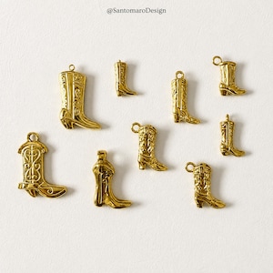 Könnte beinhalten: Eine Sammlung von acht goldfarbenen Metallanhängern in Form von Cowboystiefeln. Jeder Anhänger weist auf der Oberfläche detaillierte Prägungen auf und verfügt über eine kleine Öse an der Oberseite zur Befestigung. Die Anhänger variieren leicht in Größe.