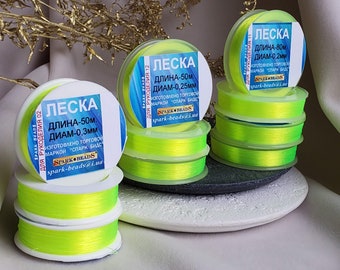 May include: Three spools of bright yellow fishing line with labels in Cyrillic script. The labels read "LESKA" which is the Russian word for fishing line. The labels also include the length and diameter of the line in millimetres. The spools are stacked on top of each other.