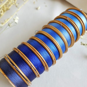 May include: A stack of blue thread spools with gold colored plastic bobbins. The spools are arranged in a spiral pattern.