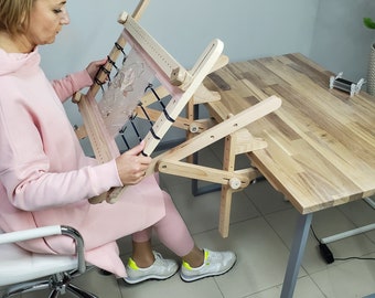 Könnte beinhalten: Ein hölzerner Stickrahmen mit verstellbaren Armen und einer Klemme, um ihn an einem Tisch zu befestigen. Der Rahmen wird verwendet, um ein Stück Stoff gespannt zum Sticken zu halten.