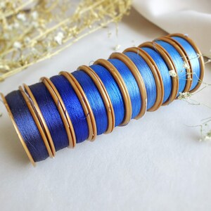 May include: A stack of blue and gold spools of thread. The spools are arranged in a circle, with the blue thread facing outwards. The spools are all the same size and have a gold trim.