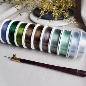 May include: A set of eight spools of clear elastic thread in various colours, including blue, green, brown, grey, and white. A wooden threader tool is also included.
