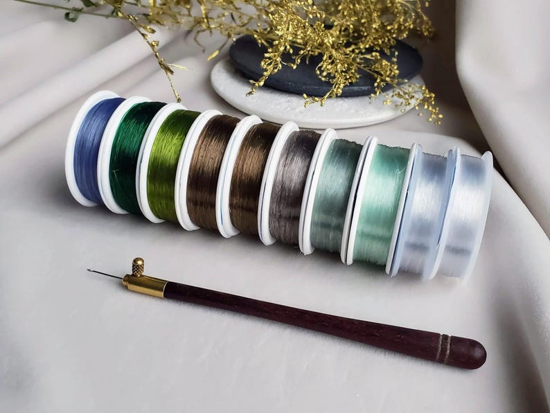 May include: A set of eight spools of clear elastic thread in various colours, including blue, green, brown, grey, and white. A wooden threader tool is also included.