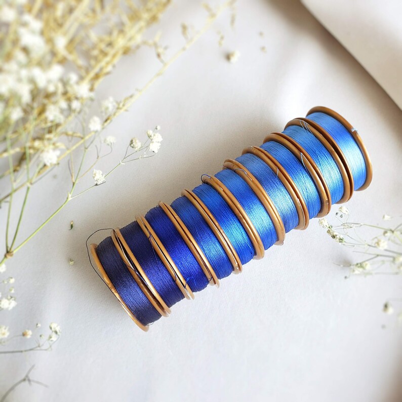 May include: A stack of blue and gold thread spools, arranged in a gradient from dark blue to light blue.