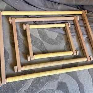 May include: A collection of wooden embroidery hoops in various sizes. The frames are made of light-colored wood with yellow, textured bars. The word "Annabecka" is printed on the yellow bars. The hoops are arranged on a gray patterned surface.