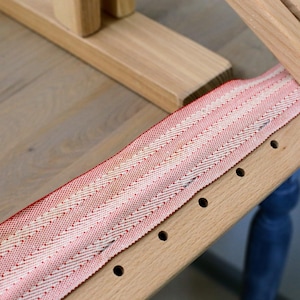 K&ouml;nnte beinhalten: Nahaufnahme eines Holzrahmens mit einem roten und wei&szlig;en gestreiften Stoff, der dar&uuml;ber gespannt ist. Der Stoff ist mit kleinen N&auml;geln befestigt und es sind L&ouml;cher in das Holz gebohrt.