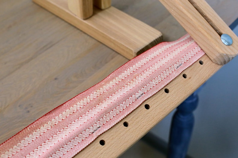 K&ouml;nnte beinhalten: Nahaufnahme eines Holzrahmens mit einem roten und wei&szlig;en gestreiften Stoff, der dar&uuml;ber gespannt ist. Der Stoff ist mit kleinen N&auml;geln befestigt und es sind L&ouml;cher in das Holz gebohrt.