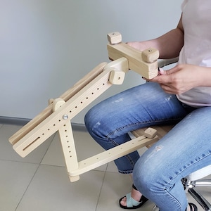 May include: A wooden adjustable armrest with a swiveling arm and a padded seat. The armrest is designed to provide support for the arm and hand while sitting in a chair.
