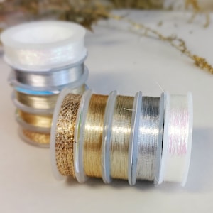 Op de afbeelding: Spoelen met gouden, zilveren en iriserende draad op doorzichtige plastic spoelen.