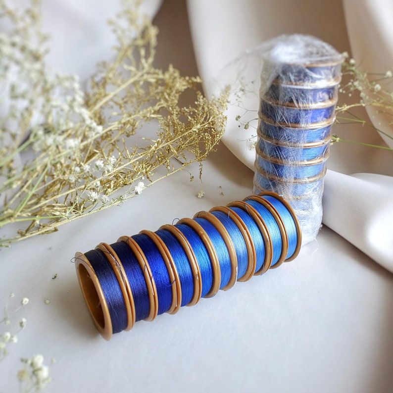 May include: A stack of blue and gold spools of thread, with a second stack of blue and gold spools of thread in the background.