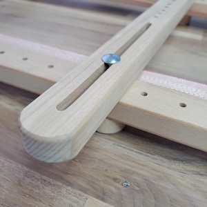 May include: Close-up of a wooden stretcher bar with a metal pin. The bar has a groove running along its length and is attached to another wooden bar.
