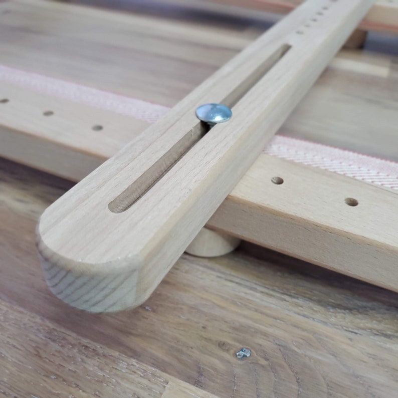 May include: Close-up of a wooden stretcher bar with a metal pin. The bar has a groove running along its length and is attached to another wooden bar.