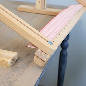 K&ouml;nnte beinhalten: Ein h&ouml;lzerner Stickrahmen mit einem rosa-wei&szlig; gestreiften Stoff, der &uuml;ber die Oberseite gespannt ist. Der Rahmen hat eine Holzbasis und zwei verstellbare Arme.