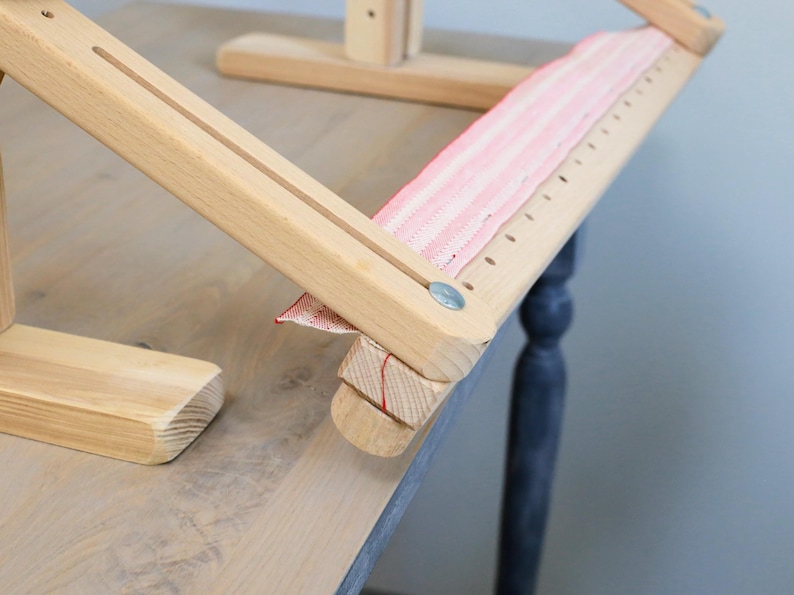 K&ouml;nnte beinhalten: Ein h&ouml;lzerner Stickrahmen mit einem rosa-wei&szlig; gestreiften Stoff, der &uuml;ber die Oberseite gespannt ist. Der Rahmen hat eine Holzbasis und zwei verstellbare Arme.