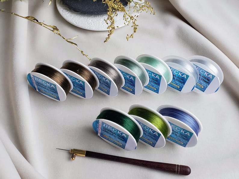 May include: Assortment of spools of clear fishing line in various colours, including brown, grey, green, and blue. Each spool is labelled with the brand name "ЛЕСКА" and the length of the line in metres.