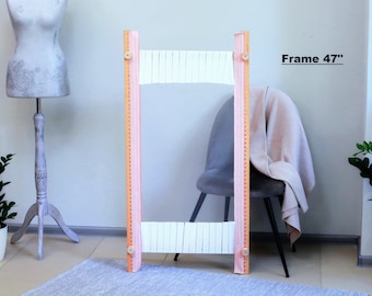 Könnte beinhalten: Ein weißer Holzwebstuhl mit rosa lackierten Seiten und einem 119 cm Rahmen. Der Webstuhl steht auf einem hellgrauen Teppich vor einem grauen Stuhl.