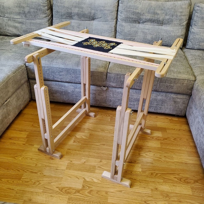 May include: A wooden embroidery stand with a white canvas stretched across it. The stand is adjustable and has a natural wood finish.