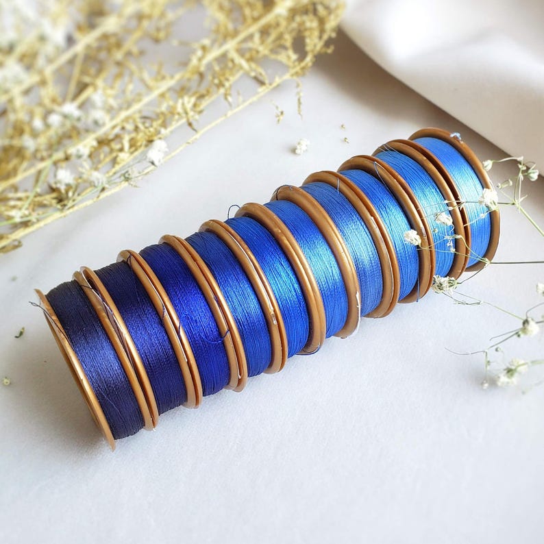 May include: A stack of spools of blue thread with gold colored plastic bobbins. The spools are arranged in a graduated size order, with the largest spool at the bottom and the smallest spool at the top.