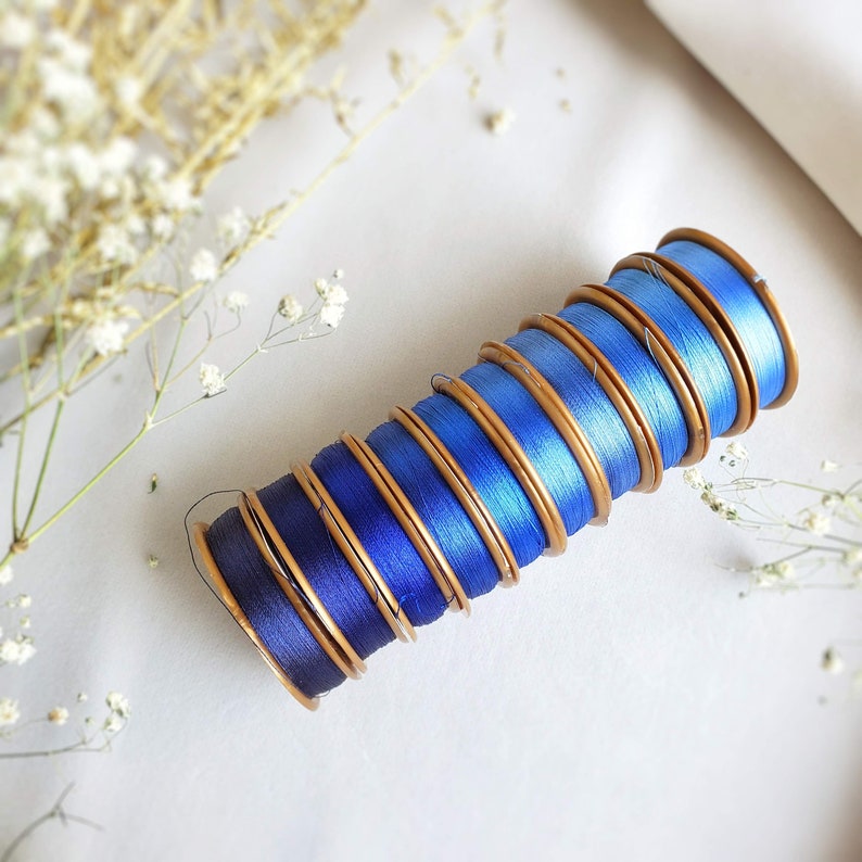 May include: A stack of blue and gold thread spools, arranged in a gradient from dark blue to light blue.