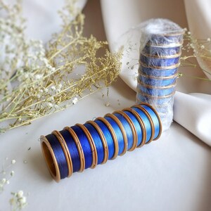 May include: A stack of blue and gold spools of thread. The spools are wrapped in blue thread and have gold trim. The spools are arranged in a stack, with the largest spool at the bottom and the smallest spool at the top.