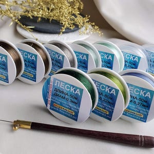 May include: An assortment of spools of clear fishing line in various colours, including green, blue, and brown. Each spool is labelled with the text "LESKA" and details about the length and diameter of the line. The text on the spools is in Russian.