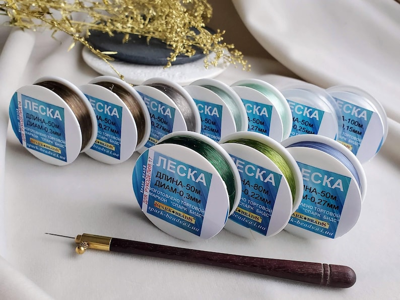 May include: An assortment of spools of clear fishing line in various colours, including green, blue, and brown. Each spool is labelled with the text "LESKA" and details about the length and diameter of the line. The text on the spools is in Russian.