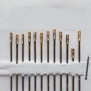 May include: A set of 12 gold-tipped needles in a white plastic case. The needles are arranged in rows and are all the same size.