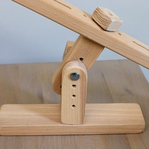 K&ouml;nnte beinhalten: Ein h&ouml;lzernes Wipptier mit naturbelassenem Finish. Die Wippe wird von einem Holzsockel mit einem Metallscharnier getragen. Die Wippe hat auf einer Seite einen kleinen Holzblock.