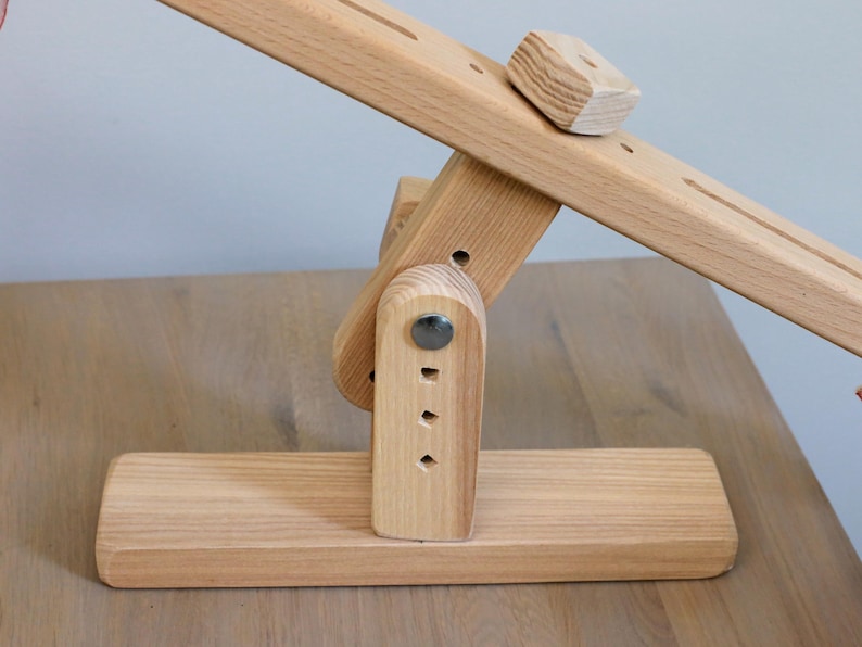 K&ouml;nnte beinhalten: Ein h&ouml;lzernes Wipptier mit naturbelassenem Finish. Die Wippe wird von einem Holzsockel mit einem Metallscharnier getragen. Die Wippe hat auf einer Seite einen kleinen Holzblock.