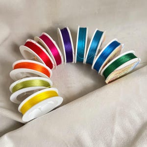 May include: A rainbow assortment of 10 spools of thread, each wound around a white plastic bobbin. The thread colors are orange, yellow, green, blue, teal, purple, pink, red, and two shades of red.