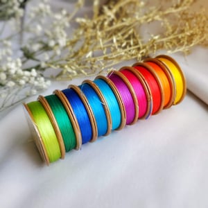 Può includere: Un set di otto bobine di filo in colori arcobaleno, disposte in una pila dal più grande al più piccolo. Le bobine sono in legno e hanno una finitura dorata.