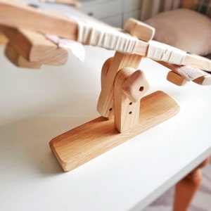 Op de afbeelding: Een houten borduurstandaard met een witte stof gespannen over de bovenkant. De standaard heeft een basis met een afgeronde rand en een mechanisme om de hoek van de stof aan te passen.