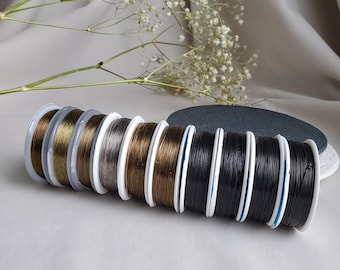 May include: A collection of spools of elastic cord in various colours, including brown, grey, and black. The spools are arranged in a row on a white surface.