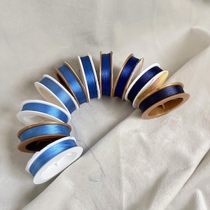 Op de afbeelding: Een verzameling spoelen met blauwe draad, gewikkeld rond witte plastic spoelen met gouden versiering. De spoelen zijn in een halve cirkel gerangschikt.