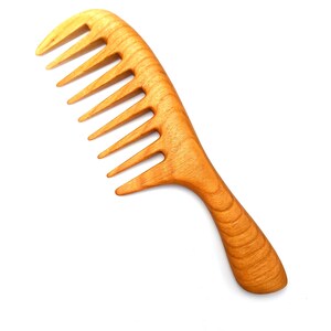 Pode incluir: Um pente de madeira com acabamento natural e uma al&ccedil;a larga e curva. O pente tem um design de dentes largos.