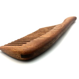 May include: A brown wooden comb with a curved handle. The comb has fine teeth and is made of natural wood.