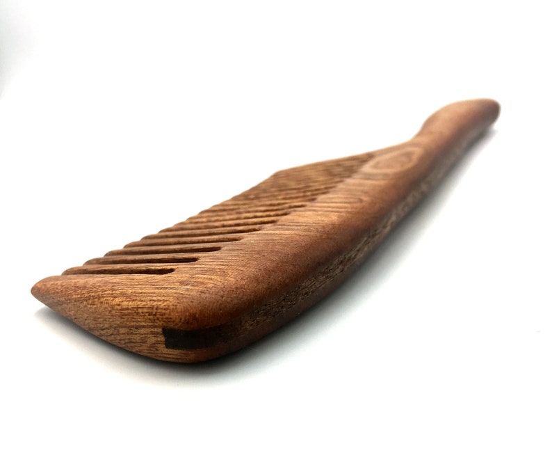 May include: A brown wooden comb with a curved handle. The comb has fine teeth and is made of natural wood.