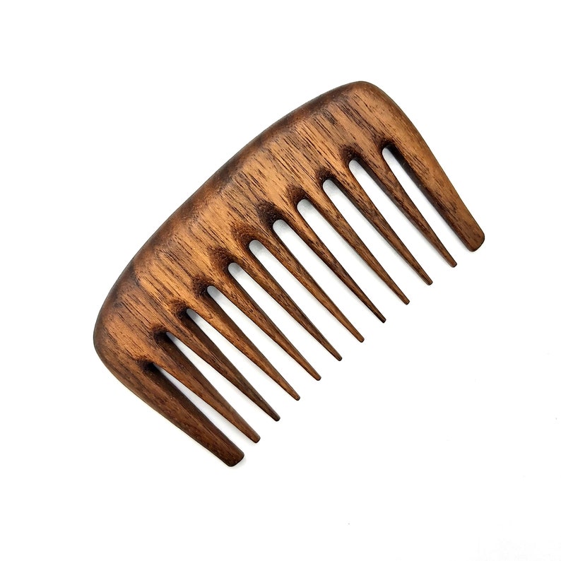 Puede incluir: Un peine de madera marr&oacute;n con un mango redondeado y siete dientes. El peine est&aacute; hecho de madera oscura y tiene un acabado natural.