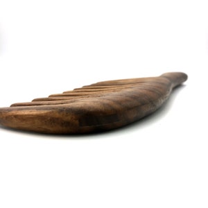 K&ouml;nnte beinhalten: Ein dunkelbrauner Holzkamm mit einem gebogenen Griff. Der Kamm hat eine nat&uuml;rliche Holzmaserung und besteht aus einem einzigen St&uuml;ck Holz.