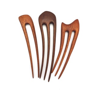 May include: Three wooden hair combs with different designs. The combs are made of dark brown and reddish-brown wood. The combs have two or three prongs.