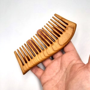 May include: A wooden comb with a curved handle and fine teeth. The comb is made of light brown wood and has a natural finish.
