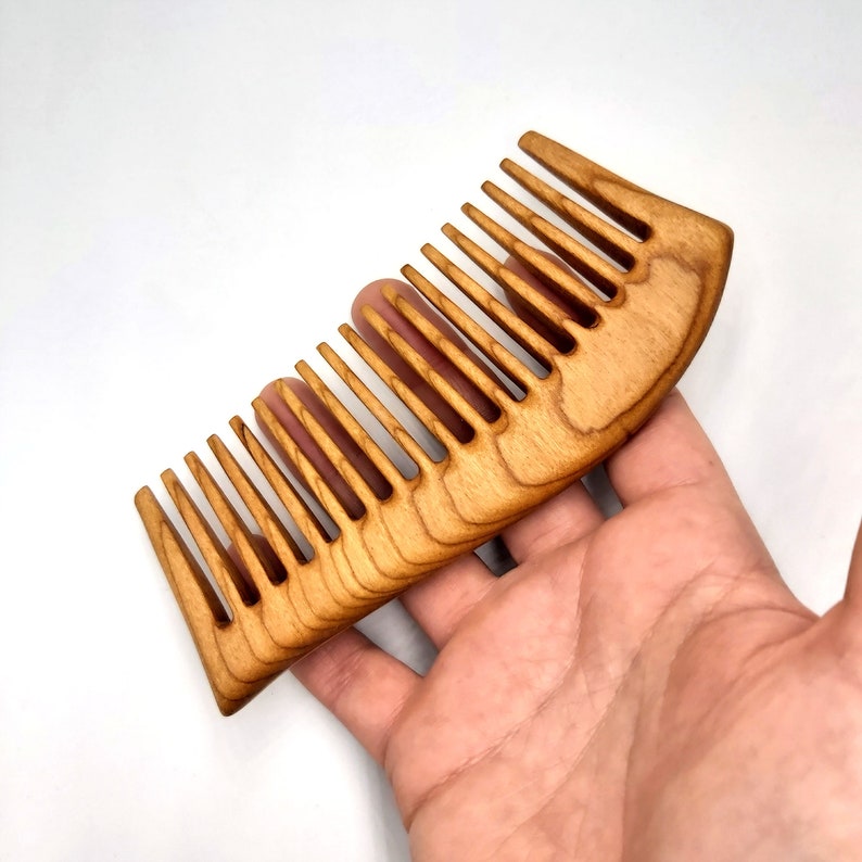 May include: A wooden comb with a curved handle and fine teeth. The comb is made of light brown wood and has a natural finish.