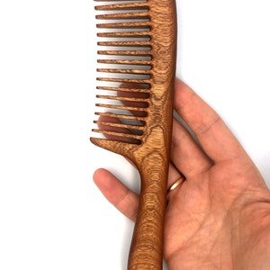 May include: A brown wooden comb with a long handle. The comb has a curved shape and is made of a dark wood with a natural grain.