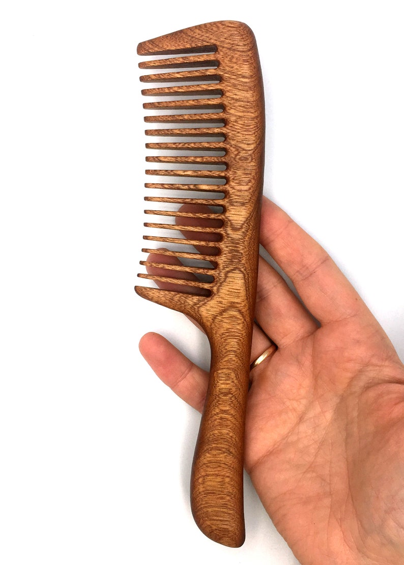 May include: A brown wooden comb with a long handle. The comb has a curved shape and is made of a dark wood with a natural grain.
