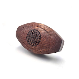 May include: A wooden, oval-shaped object with a dark brown finish. The object has a laser-etched flower of life design in the centre. The object is about 7.5 cm long.